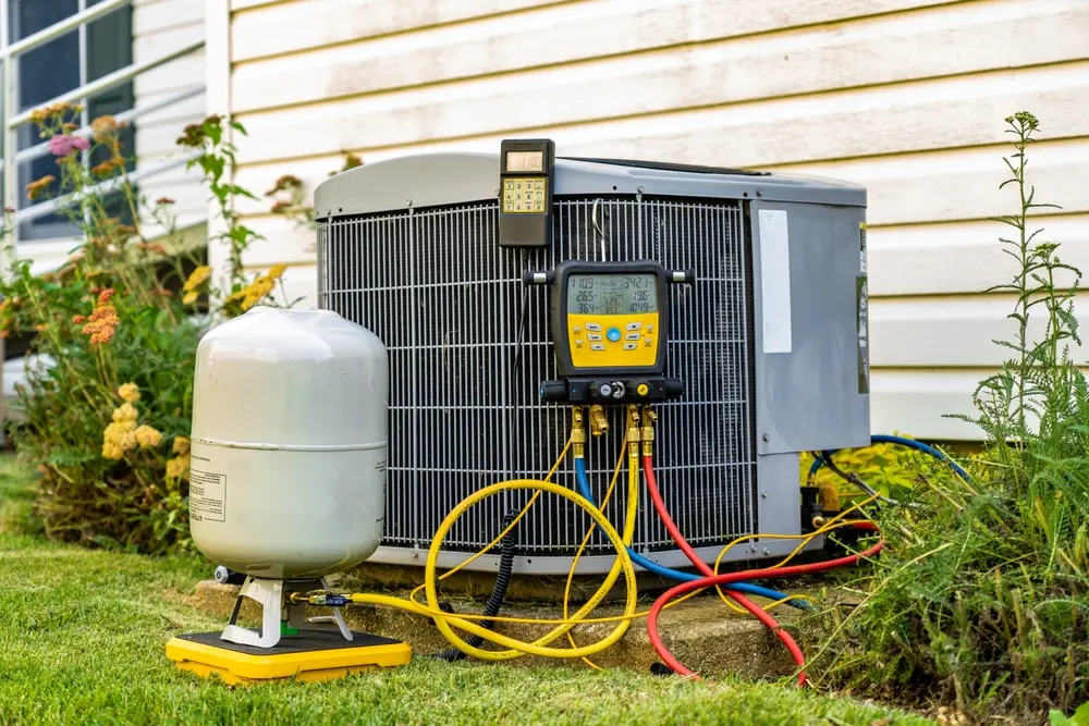 An old air conditioning unit that is being repaired by an HVAC service technician. The technician is using digital refrigerant gauges, and a digital scale.