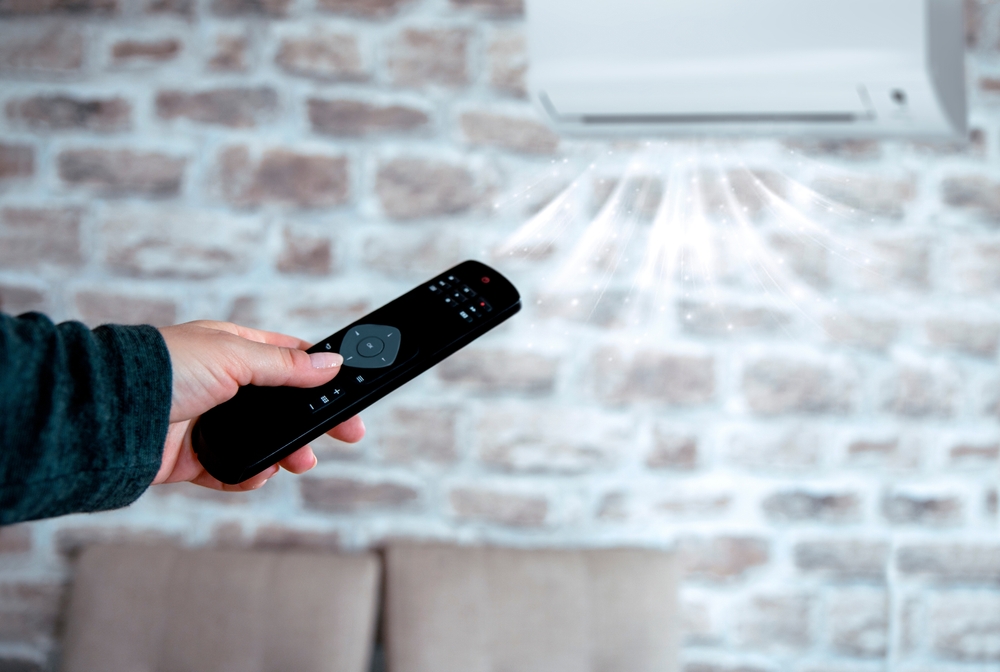 Black Remote control in female hand controlling air conditioner temperature. Close up background. ductless mini split zoning control systems.